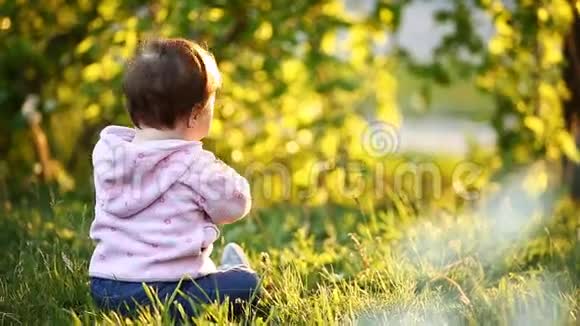 后景可爱的女婴坐在公园里的绿草上日落视频的预览图