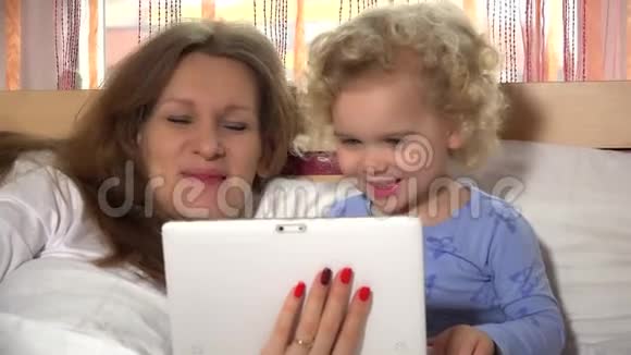 快乐的孩子和妈妈保姆在床上玩平板电脑视频的预览图