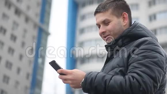 冬天的男人在聊天社交媒体上拨打一条信息男人在室外手持智能手机多层楼视频的预览图