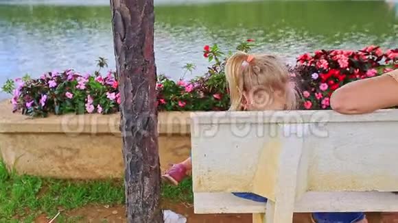 金发母亲小女孩坐在长凳上看湖背视频的预览图