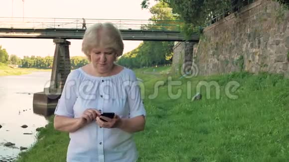 老年妇女使用智能手机沿着海滨散步桥和复古墙的野石背景视频的预览图