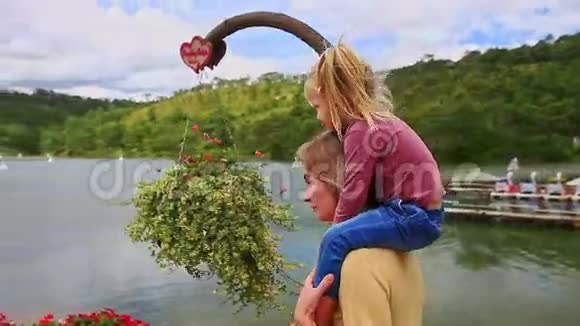 母亲把小女孩抱在肩上在湖边岸边散步视频的预览图