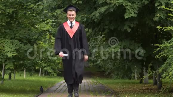 快乐的男毕业生在公园里散步快乐地跳跃成功和未来视频的预览图