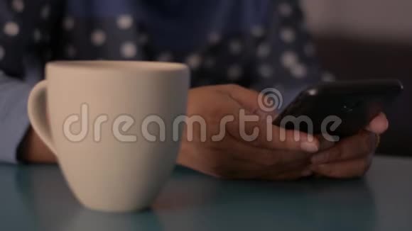 女人在桌子上用智能手机在家里喝一杯咖啡打字短信视频的预览图