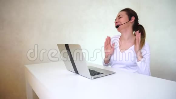 年轻的金发女人扎着马尾辫坐在桌子旁边在光线充足的房间里拿着银色的笔记本电脑接电话视频的预览图
