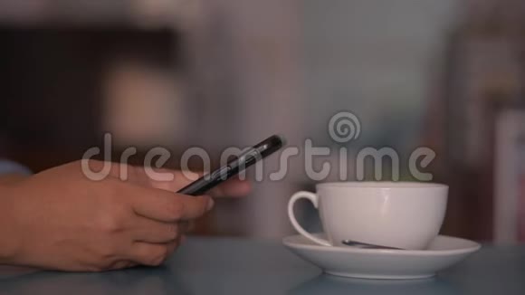 女人在桌子上用智能手机在家里喝一杯咖啡打字短信视频的预览图