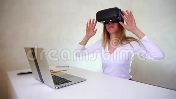 年轻女子坐在桌子旁拿着银色笔记本电脑测试虚拟现实眼镜视频的预览图