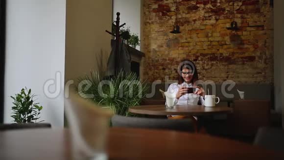 智能手机女孩在手机上使用应用程序在咖啡馆里微笑地喝咖啡美丽的多元文化年轻休闲女性视频的预览图