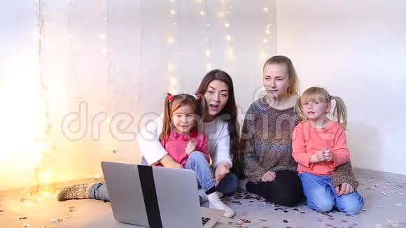 两个漂亮的妈妈带着小女儿坐在地板上通过视频电话与家人交流视频的预览图