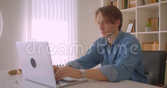 年轻有魅力的高加索商人用笔记本电脑在办公室室内观看照相机的特写照片视频的预览图