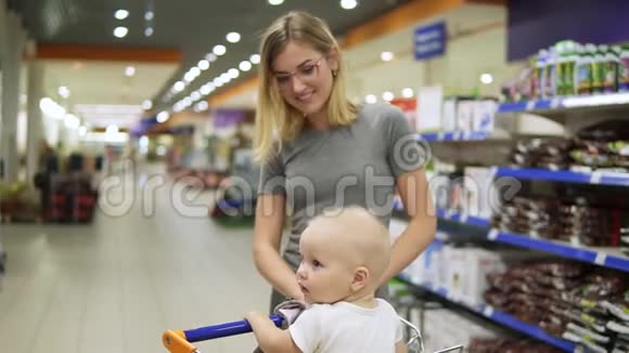 年轻的母亲带着她的小宝宝坐在超市的购物车里正推着购物车向前走视频的预览图