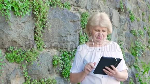 使用带有耳机的平板电脑的老年妇女背景中野生石头的复古墙视频的预览图