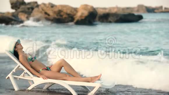 年轻漂亮的晒黑的女人长发披着比基尼躺在沙滩躺椅上视频的预览图