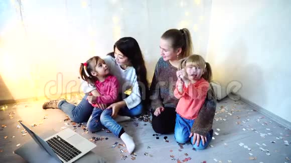 老年妇女与年幼的女童和姐妹在一起使用笔记本电脑坐在地板上背景视频的预览图