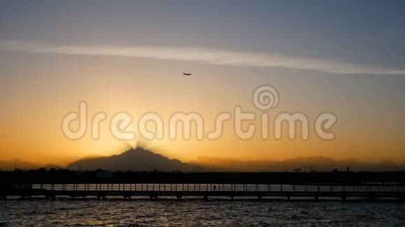 飞机飞过夕阳飞过高山光线穿过黄昏的薄雾平静的大海和码头视频的预览图