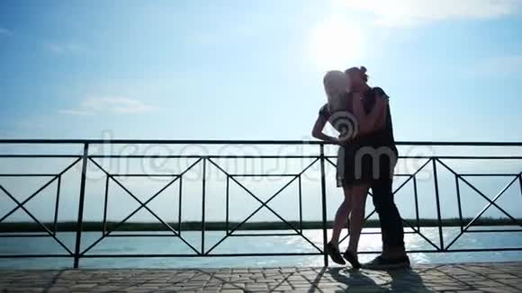 一个男人在阳光下拥抱亲吻他的女朋友一对可爱的情侣站在湖边视频的预览图