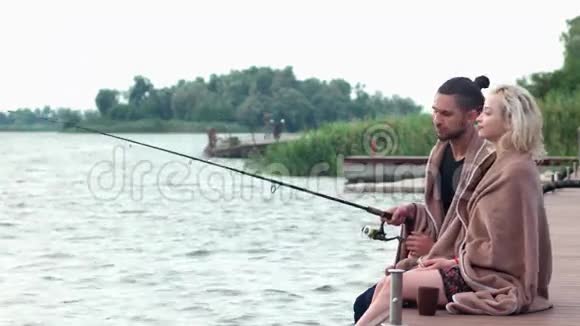 可爱的一对夫妇在码头钓鱼早上喝咖啡恋人们在河边的码头喝热茶视频的预览图