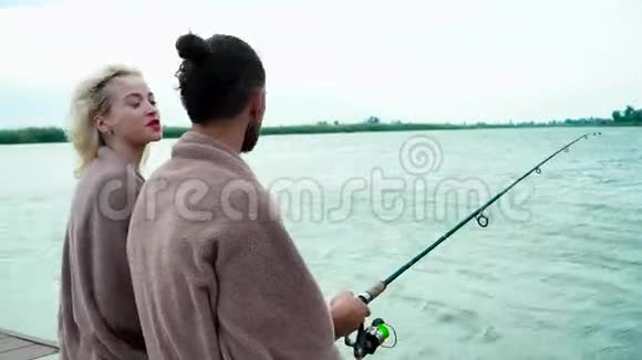 一对夫妇在湖边钓鱼风吹着头发男孩和女孩一边聊天一边钓鱼视频的预览图