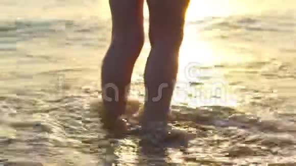 孩子的脚站在海边在海浪中在夕阳的背景下视频的预览图