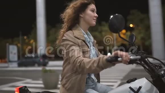 美丽的年轻女子骑着一辆古老的咖啡馆赛车摩托车在街上晚上的女自行车手慢动作视频的预览图