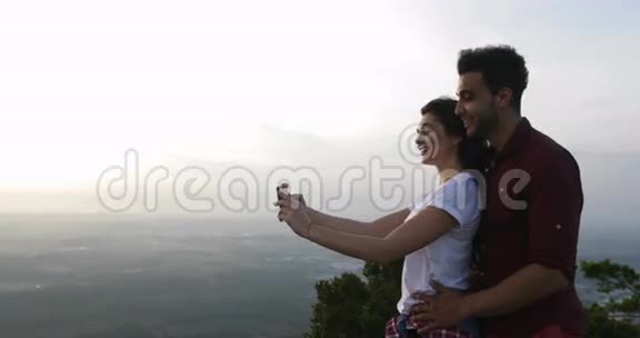 山顶情侣在手机上自拍男人和女人在日出时拥抱快乐的微笑视频的预览图