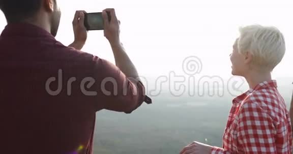 男子手机拍照日出景观山顶情侣后景视频的预览图