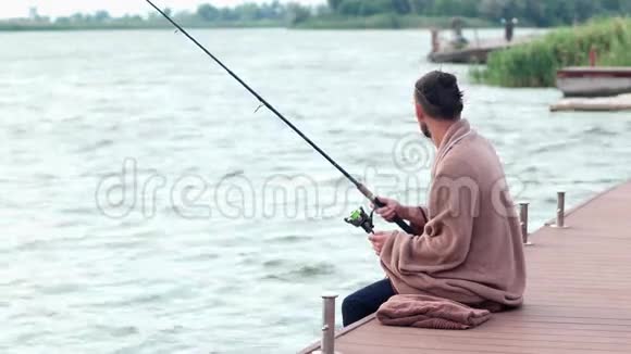 男人在湖边钓鱼男人在码头上用鱼竿坐着钓鱼女孩带着热茶爱人视频的预览图