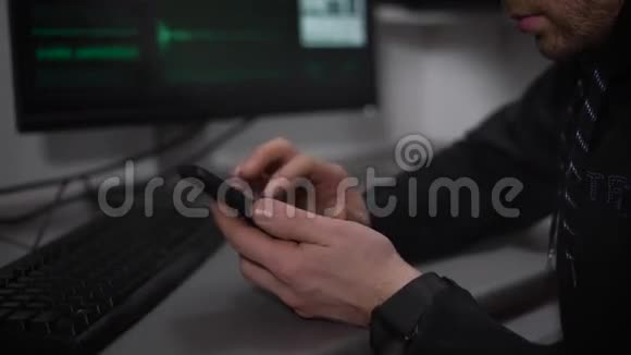 关闭坐在桌子旁使用智能手机的俄罗斯黑客男性间谍正在用电脑系统入侵视频的预览图