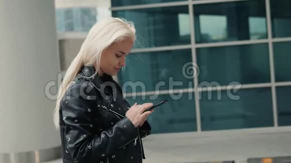 美丽的女人在走在街头模特金发的时候正在用智能手机上的应用程序发送一条短信视频的预览图