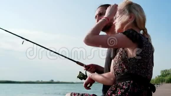 年轻浪漫的情侣坐在河边的码头上钓鱼恋人们在阳光下钓鱼视频的预览图