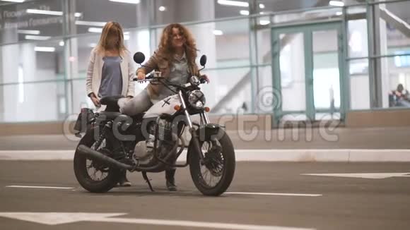 美丽的年轻女子摩托车手和他的女朋友骑摩托车在一个夜间城市的灯光街道两个骑自行车的女人视频的预览图