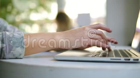 女性手在笔记本电脑上工作的特写镜头女人坐在靠近窗户的咖啡馆里打字白色杯子视频的预览图