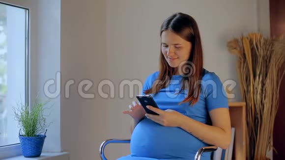 孕妇坐在家里客厅的沙发上用手机发短信视频的预览图