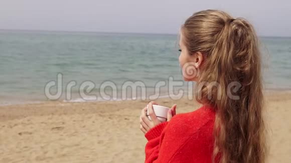 金发女孩在海边的海滩上喝茶视频的预览图
