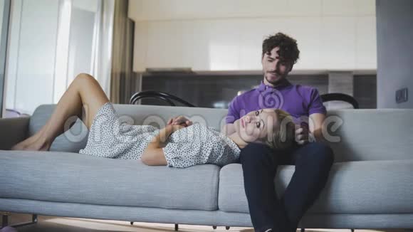 千禧一对相爱的夫妇在家里的沙发上放松幸福的夫妻互相看着笑了起来视频的预览图
