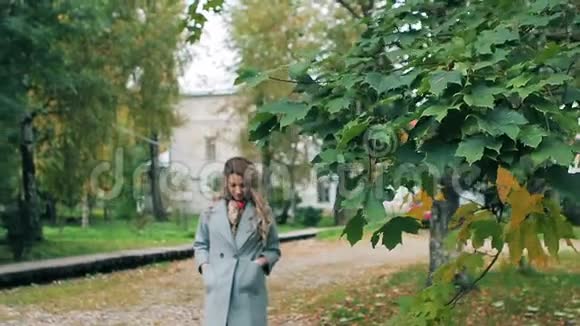 穿灰色衣服的女孩走在枫树绿树旁摆出秋天的姿态视频的预览图