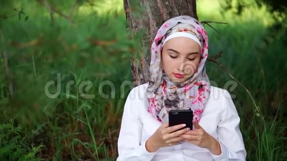 一个戴头巾的穆斯林和朋友通电话她坐在公园里视频的预览图