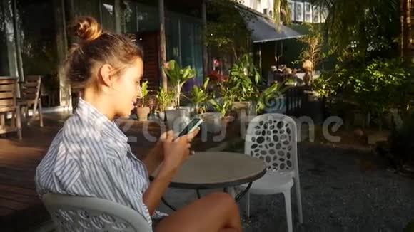 可爱的白种人年轻女人坐在咖啡馆里在电话上写留言视频的预览图