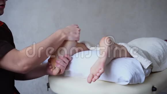 英俊的练习按摩师揉捏女性客户的脚她躺在明亮的医疗沙龙沙发上视频的预览图