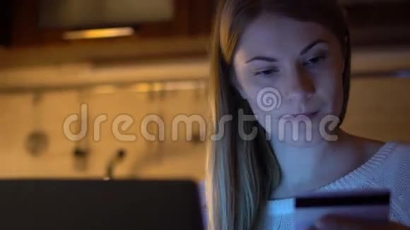 美丽迷人的女人晚上在厨房用笔记本电脑在线购买信用卡视频的预览图