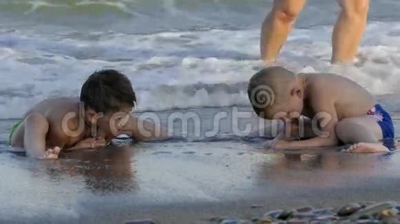 男孩们坐在海滩上享受着海浪和沙子玩耍慢动作视频的预览图