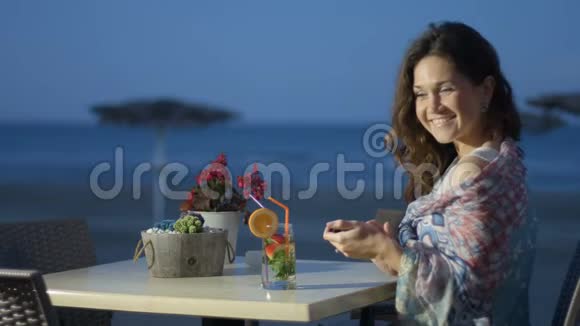 漂亮的女人在手机上发短信脸上带着微笑在海边咖啡馆休息视频的预览图