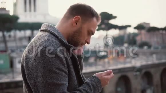 时髦的人站在意大利罗马的中心帅哥用智能手机浏览互联网视频的预览图
