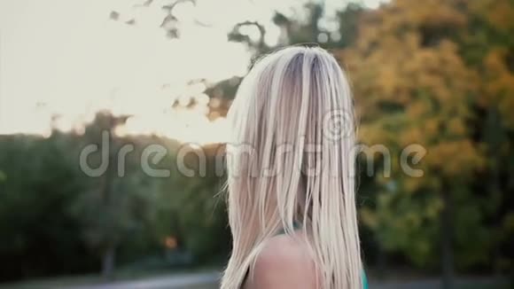 日落公园里美丽的年轻女子的肖像金发女孩转过身来看着相机她的头发波浪慢动作视频的预览图