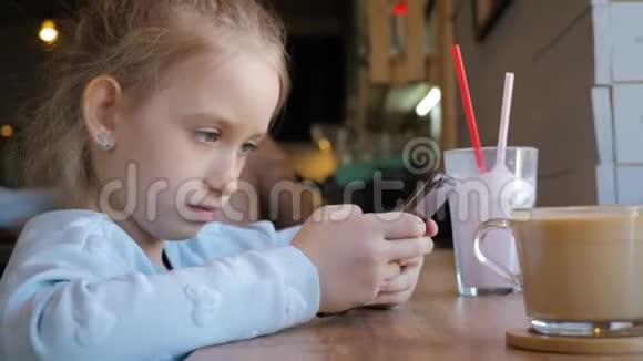 可爱的小女孩在咖啡馆里用智能手机快乐的孩子在放学后玩得开心和放松自然室内视频的预览图