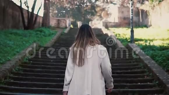 年轻的黑发女孩上楼梯时髦的女人走在春天的老城明亮的阳光在早晨视频的预览图
