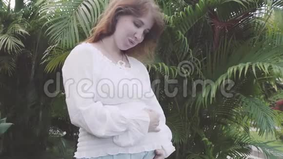 孕妇抚摸着她的小肚子在公园里的树间行走视频的预览图