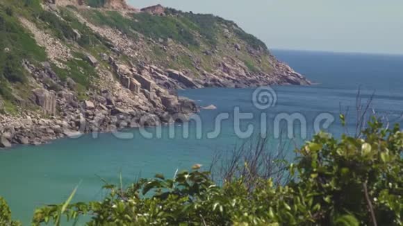 海岛上的岩石悬崖和碧水景观绿色的海岛岩石海岸和碧水在清晰的天际线上视频的预览图