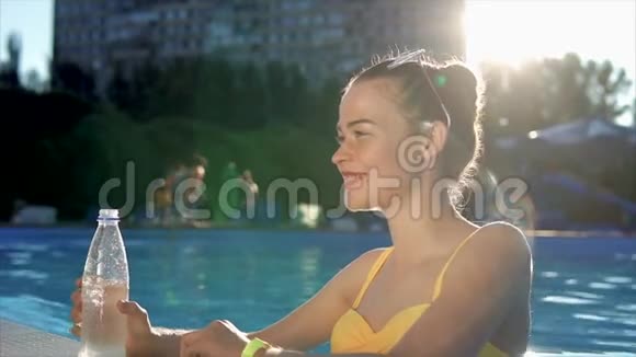 穿着泳衣的年轻女子从游泳池里的塑料瓶里喝凉水视频的预览图