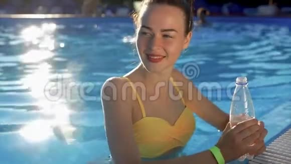 穿着泳衣的年轻女子从游泳池里的塑料瓶里喝凉水视频的预览图